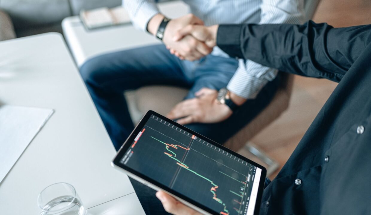Two people shaking hands over a financial graph on a tablet to seal a business agreement