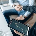 Two people shaking hands over a financial graph on a tablet to seal a business agreement