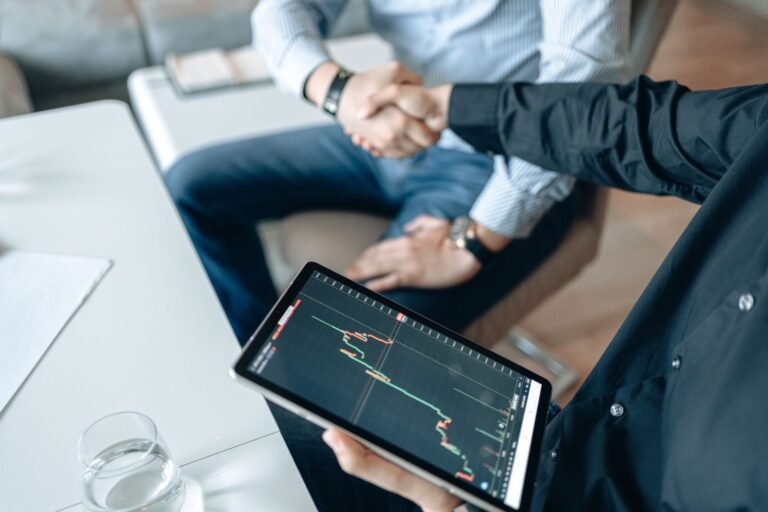 Two people shaking hands over a financial graph on a tablet to seal a business agreement